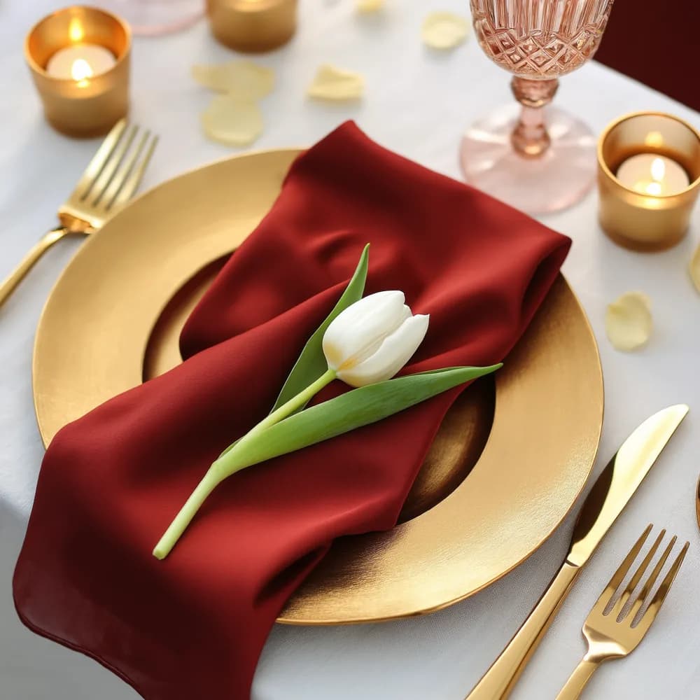 A place setting with a gold charger, crimson napkin and a white tulip